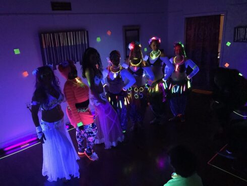 Image of a room with black light showing belly dancers