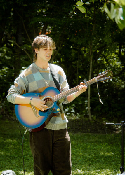 photo of a musician playing a guitar, wearing a checkered sweater