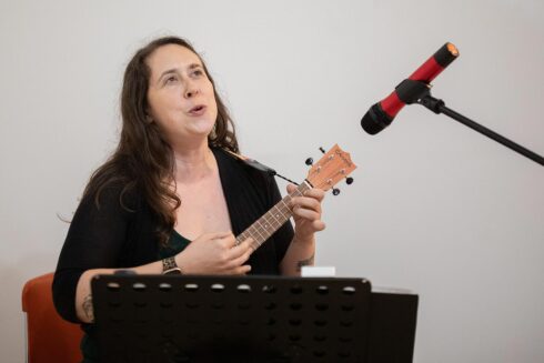 Image showing Pamela Draper singing, with a smile on her face and playing a cahaya ukulele
