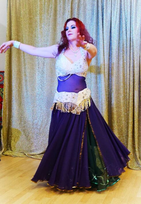 Belly dancer with red hair a dark purple skirt and cream dress